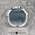 The Mooney, Mia and Wight, Spencer 2 ring—a silver band with a rough blue gemstone—rests on a geometric-patterned surface above the “Earth’s Treasury” text, capturing Guinevere-like elegance.