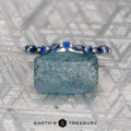 A Mock, Eli and Herbert, Olivia 2 ring—silver with oval and round sapphires—rests on a rough blue crystal atop a geometric patterned background, with "EARTH'S TREASURY" beneath.
