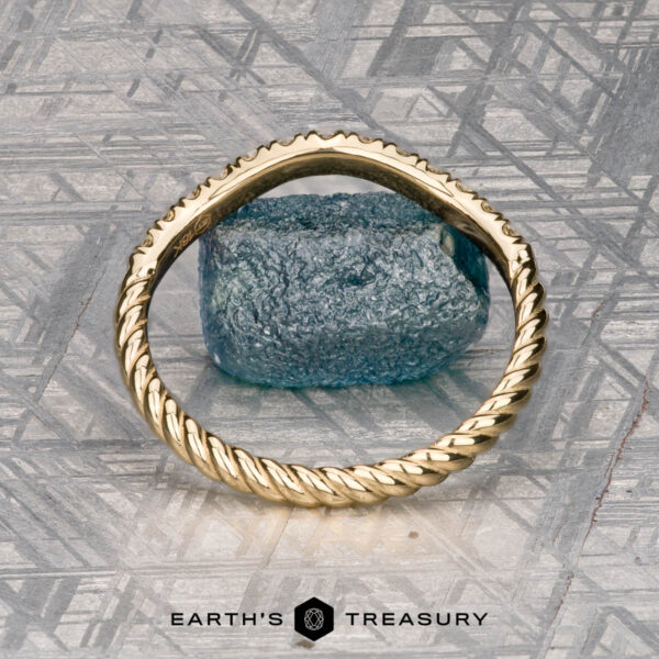The Contour "Lynn" band in 18k yellow gold A gold Obendorf, Kenny and Kitchin, Amelia 2 ring with a rough blue gemstone rests on a metallic patterned surface, with "EARTH’S TREASURY" written below.