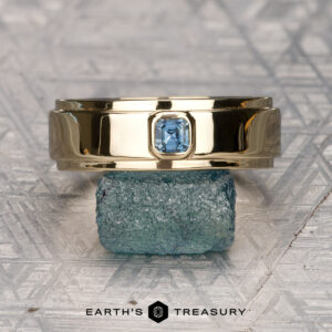 A gold "Stacked from 16 images. Method=B (R=10,S=7)" Sapphire Ring with a rectangular blue gemstone is balanced on a rough blue stone, against a textured background, with the text "Earth's Treasury" below.