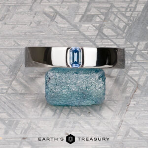 The Harrison, Samuel 3 ring features a rectangular blue gemstone set in silver, displayed upright on a rough Elgon blue stone with the "EARTH'S TREASURY" logo and text underneath.