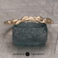 The "Linden" band in 14K yellow gold, featuring a delicate leaf design, is displayed atop a rough blue gemstone with the text "EARTH'S TREASURY" below.
