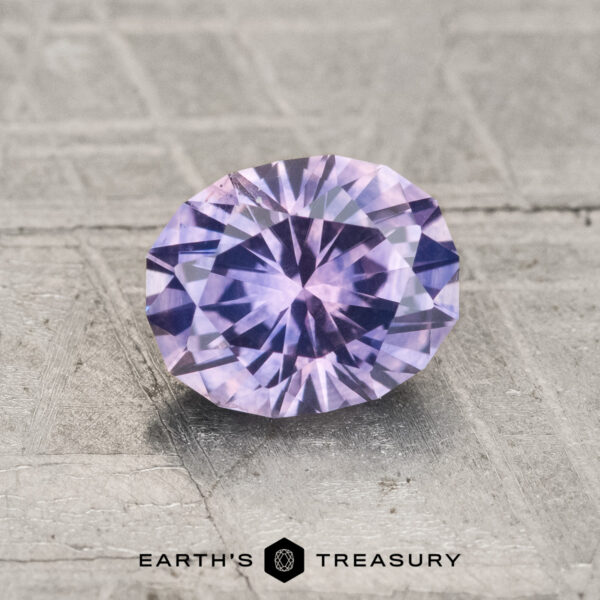 1.37-Carat Montana Sapphire (Heated) A 1.37-carat heated Montana Sapphire gemstone is displayed on a textured gray surface, with “EARTH'S TREASURY” and a geometric logo beneath it.
