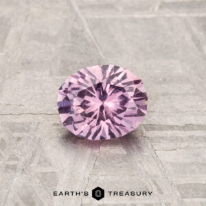 A 0.68-carat Montana Sapphire, round brilliant-cut, is displayed on a textured gray surface with the text "Earth's Treasury" at the bottom.