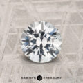 A 1.52-carat round brilliant-cut Montana Sapphire is shown on a textured gray surface with "EARTH'S TREASURY" displayed at the bottom.