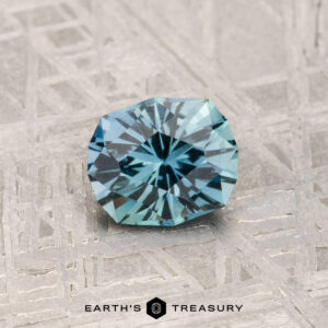 A faceted 0.82-carat Montana Sapphire with intricate cuts is displayed on a patterned metallic surface, with the text "Earth's Treasury" at the bottom.