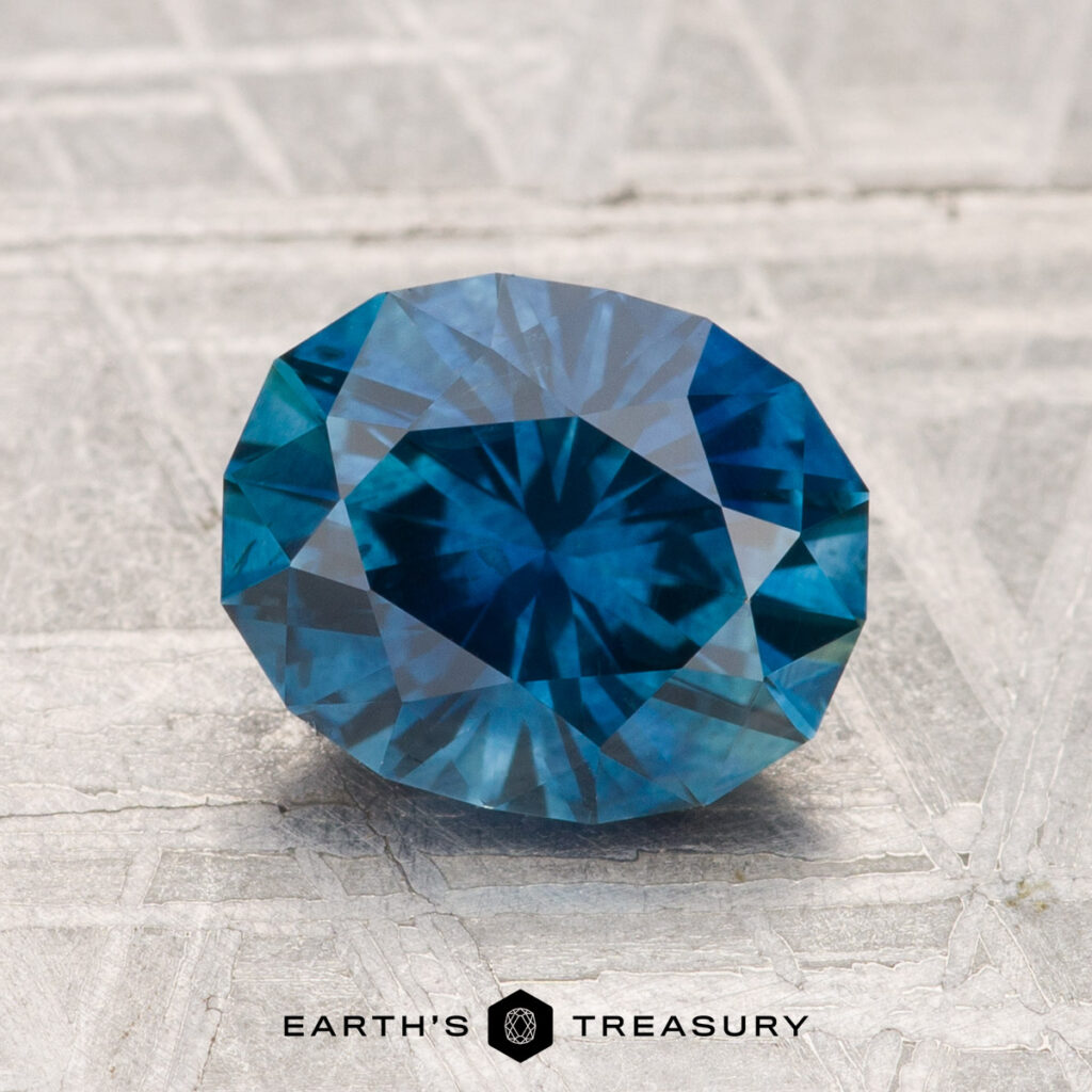 A 2.16-carat heated Montana sapphire, faceted in an oval shape, displayed on a textured gray surface with the "Earth's Treasury" logo at the bottom.