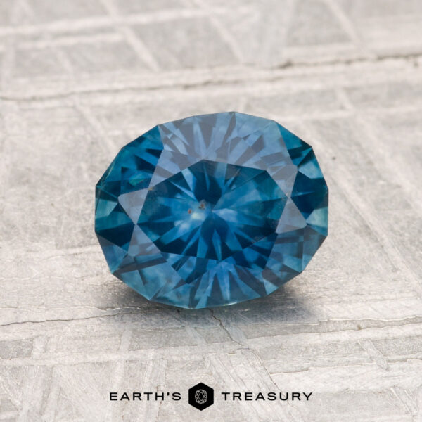 1.57-Carat Montana Sapphire (Heated) A 1.57-carat heated Montana sapphire is displayed on a textured gray surface with the text "EARTH'S TREASURY" below it.