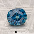 A 2.02-carat heated Montana sapphire is displayed on a textured gray surface with "EARTH'S TREASURY" at the bottom.