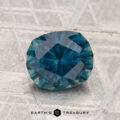 A 1.98-carat heated Montana sapphire with blue-green facets is displayed on a textured gray surface, with "EARTH'S TREASURY" text at the bottom.
