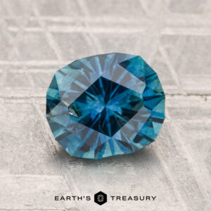 A 1.96-carat heated Montana sapphire with visible inclusions is shown on a textured gray surface, with "EARTH'S TREASURY" at the bottom.