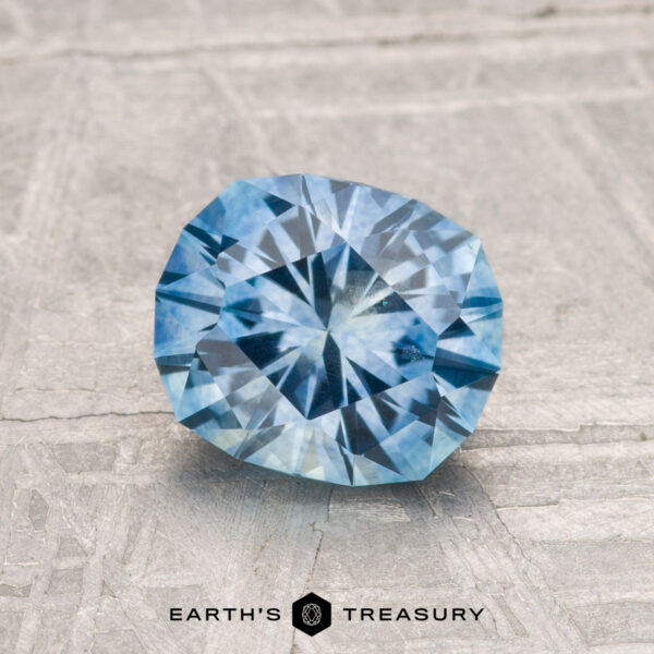 1.51-Carat Montana Sapphire (Heated) A 1.51-carat heated Montana sapphire with a cushion cut is displayed on a textured gray surface. The Earth's Treasury logo appears at the bottom.