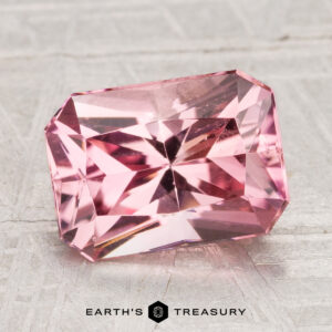 A rectangular, faceted 3.02-carat California Tourmaline gemstone rests on a light-colored textured surface, with the text "EARTH'S TREASURY" below.