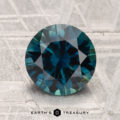 A 2.30-carat heated Montana Sapphire gemstone, round and blue-green with facets, is displayed on a textured gray surface with "EARTH'S TREASURY" below.