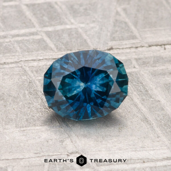 1.07-Carat Montana Sapphire (Heated) A 1.07-carat heated Montana sapphire with round, faceted cuts is shown on a textured gray surface, featuring "EARTH'S TREASURY" at the bottom.