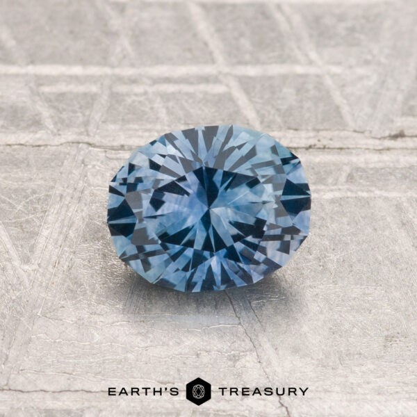 0.92-Carat Montana Sapphire (Heated) A 0.92-carat, round, faceted Montana sapphire (heated) is showcased on a textured metallic surface with "EARTH'S TREASURY" displayed at the bottom.