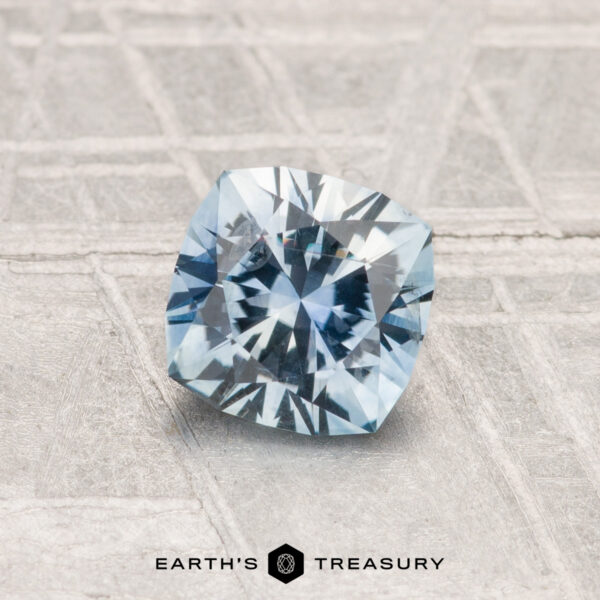 1.00-Carat Montana Sapphire (Heated) A 1.00-carat heated Montana sapphire, cushion-cut and blue, is displayed on a textured gray surface with "EARTH'S TREASURY" at the bottom.