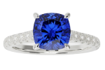 The ring-classic features a silver band with a large cushion-cut blue gemstone at the center, accented by small clear stones along the band.