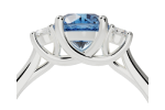 Side view of the ring-trellis: a silver ring with a central blue gemstone, two smaller clear stones on each side, all set in an intricate prong setting.