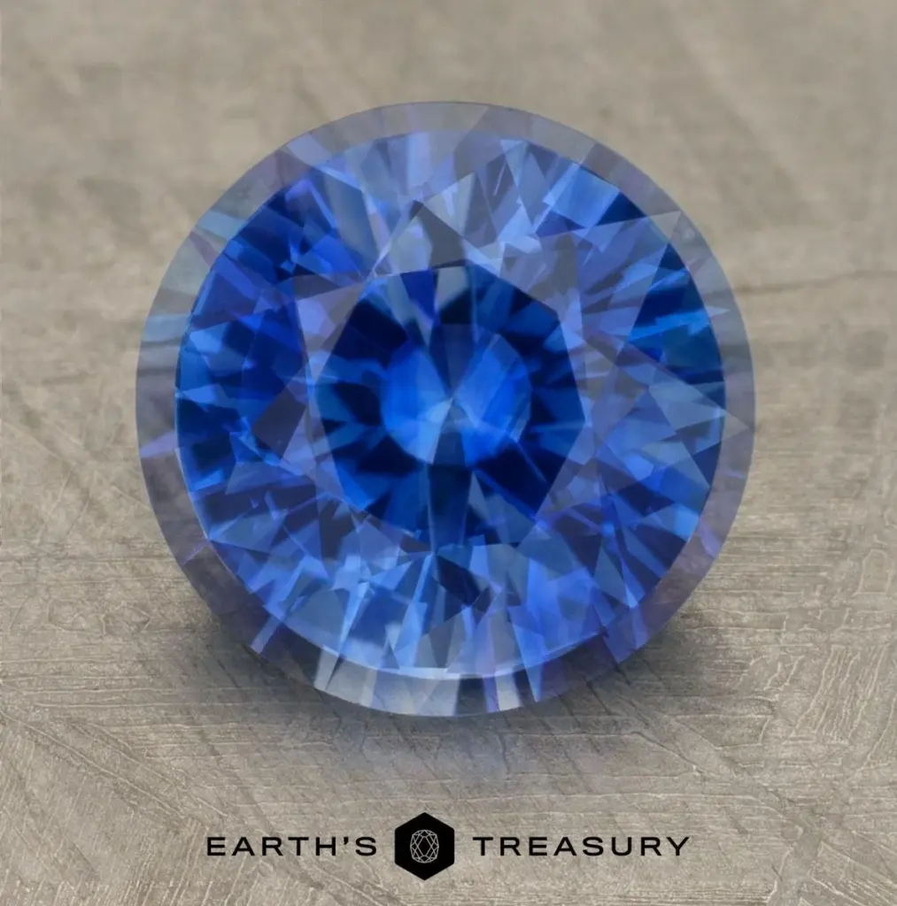 Round brilliant-cut sapphire showcased on a textured surface, with "Earth's Treasury" logo and the product name "sapphire-before-and-after-precision-cutting-v0-yox9bwylhwbf1" displayed at the bottom.