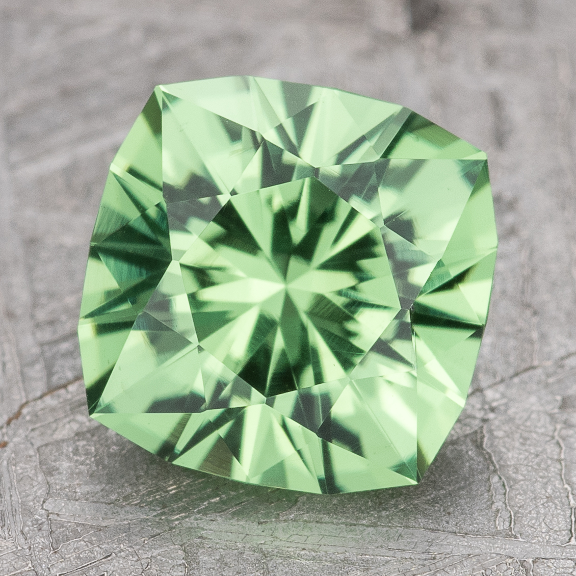 The Garnet-Green gemstone, featuring square cuts and detailed facets, rests on a textured gray surface.