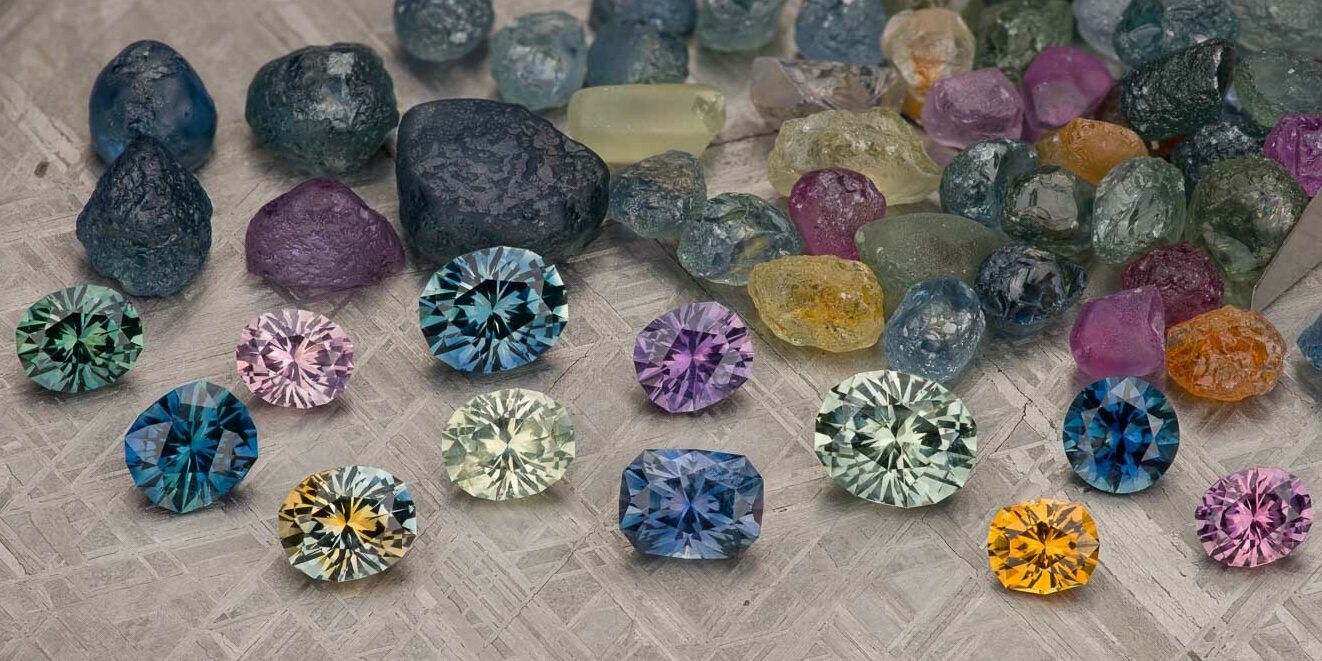 Stacked from 19 images. Method=B (R=9,S=5): A selection of rough and faceted gemstones in various colors displayed on a textured gray surface.