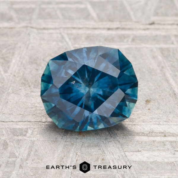 1.75-Carat Montana Sapphire (Heated) A faceted, oval 1.75-carat Montana Sapphire (heated) is showcased on a textured gray surface with "EARTH'S TREASURY" text at the bottom.