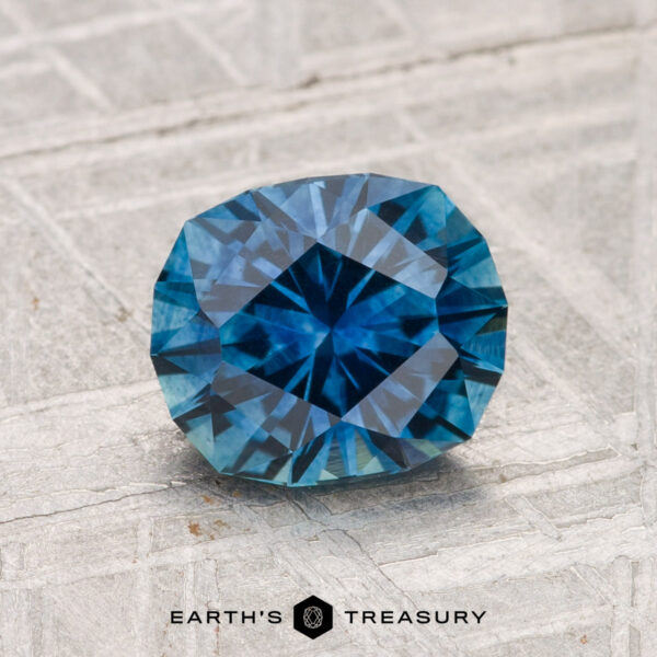 1.64-Carat Montana Sapphire (Heated) A 1.64-carat heated Montana sapphire with a cushion cut is showcased on a textured light gray surface, with "EARTH'S TREASURY" visible at the bottom.