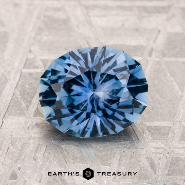 2.03-Carat Montana Sapphire A round, brilliantly cut 2.03-carat Montana Sapphire in medium blue is displayed on a geometric patterned surface, with the text "EARTH'S TREASURY" at the bottom.