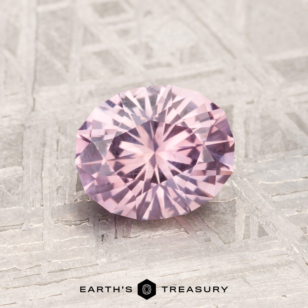 A 1.39-carat, round, faceted Montana sapphire in light purple rests on a textured metallic surface, with "EARTH'S TREASURY" displayed below.