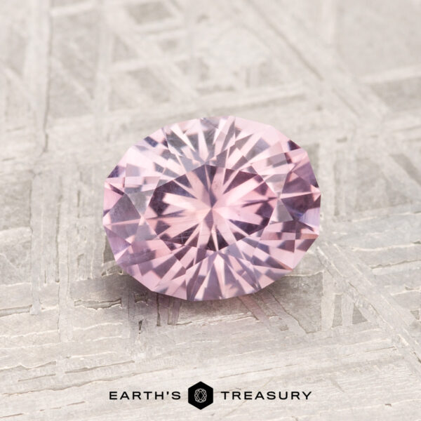 1.39-Carat Montana Sapphire A 1.39-carat, round, faceted Montana sapphire in light purple rests on a textured metallic surface, with "EARTH'S TREASURY" displayed below.
