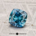 A 1.40-carat heated Montana sapphire with a cushion cut rests on a textured gray surface, with "EARTH'S TREASURY" displayed at the bottom.