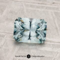 A 1.73-carat rectangular, faceted Montana Sapphire (heated) with a light blue hue is shown on a textured pale surface, with "Earth's Treasury" displayed below.