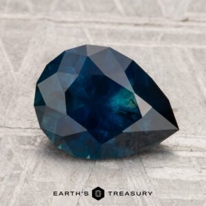 A 2.53-carat heated Montana sapphire, faceted in a pear shape, is displayed on a textured light surface with the Earth’s Treasury logo below.