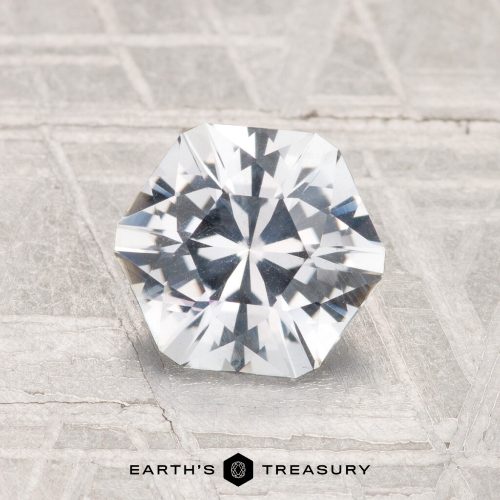 A faceted, octagonal 1.49-carat Montana Sapphire rests on a textured light gray surface with the "Earth's Treasury" logo and text at the bottom.