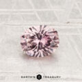 A 0.86-carat Montana sapphire, faceted in an oval shape with a pink hue, is displayed on a textured light-gray surface with "EARTH'S TREASURY" at the bottom.