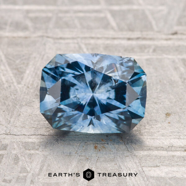 1.99-Carat Montana Sapphire (Heated) A rectangular, faceted 1.99-carat heated Montana sapphire rests on a gray textured surface with "EARTH'S TREASURY" displayed below.