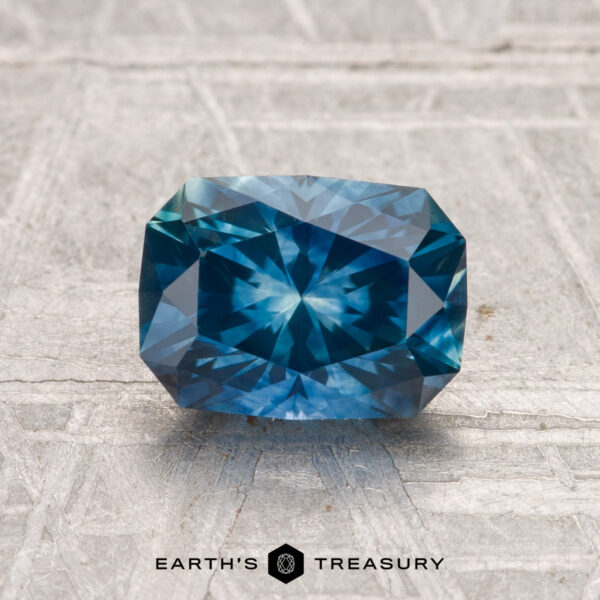 A 1.70-carat heated Montana Sapphire with a cushion cut is shown on a textured gray surface, with "EARTH'S TREASURY" written below.