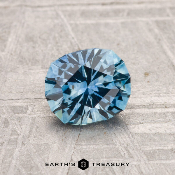 1.16-Carat Montana Sapphire (Heated) A 1.16-carat heated Montana sapphire with oval radiant cuts is displayed on a textured light gray surface. The Earth's Treasury logo appears at the bottom of the image.