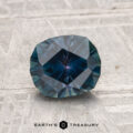 A 1.53-carat heated Montana sapphire with a deep blue hue is shown on a textured gray surface, featuring the text "EARTH'S TREASURY" at the bottom.