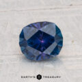 A faceted, deep blue 1.53-carat heated Montana Sapphire with an oval cut rests on a light, textured surface. The "EARTH'S TREASURY" logo appears at the bottom of the image.