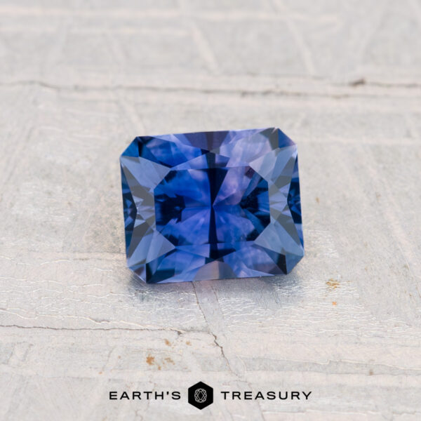 0.80-Carat Montana Sapphire (Heated) A rectangular, deep blue 0.80-carat heated Montana sapphire with intricate faceting rests on a light textured surface; the "Earth's Treasury" logo appears at the bottom.
