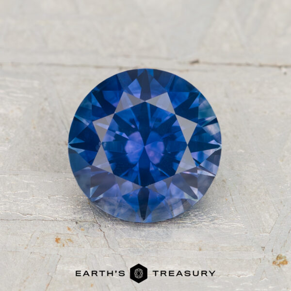 1.72-Carat Montana Sapphire (Heated) A 1.72-carat heated Montana sapphire, round brilliant-cut and blue, is displayed on a light textured surface with "EARTH'S TREASURY" below.