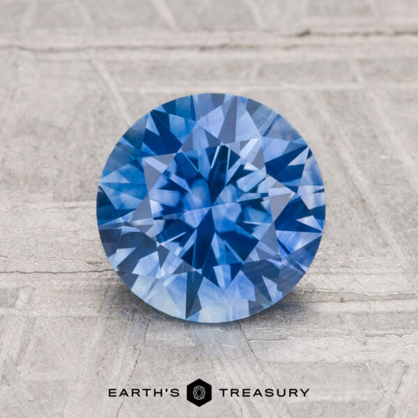 2.00-Carat Montana Sapphire (Heated) A 2.00-carat round brilliant-cut heated Montana Sapphire is displayed on a light textured surface with "EARTH'S TREASURY" below.