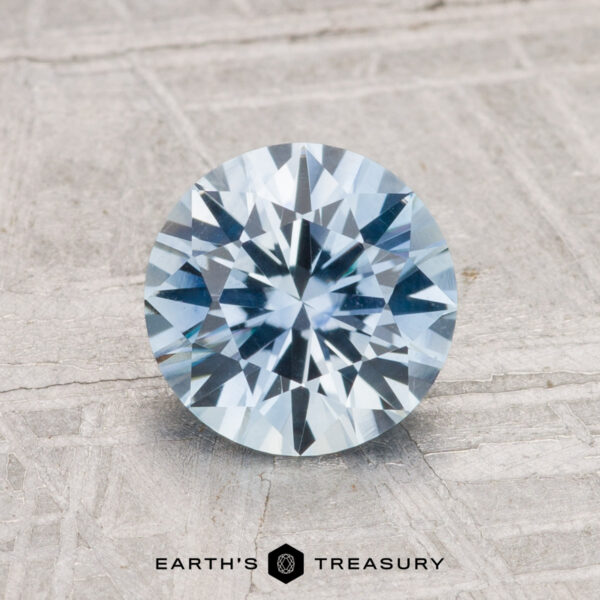 1.64-Carat Montana Sapphire (Heated) A 1.64-carat heated Montana sapphire, round brilliant-cut and blue in color, is shown on a gray textured surface with "EARTH'S TREASURY" written below.