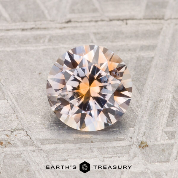 1.18-Carat Montana Sapphire (Heated) A 1.18-carat heated Montana sapphire with a peachy-pink hue is shown on a textured metallic surface, featuring "EARTH'S TREASURY" at the bottom.