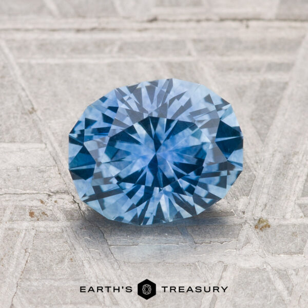 1.91-Carat Montana Sapphire (Heated) A 1.91-carat oval-cut Montana sapphire (heated) is displayed on a textured gray surface with the text "EARTH'S TREASURY" beneath it.