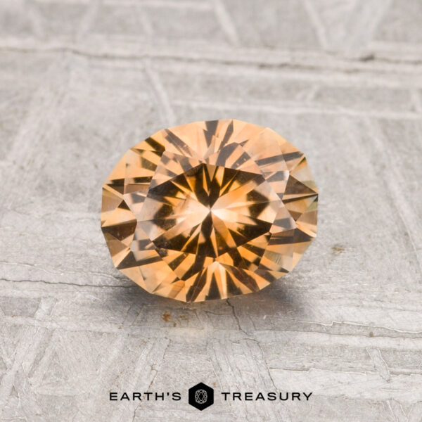 1.37-Carat Montana Sapphire (Heated) A 1.37-carat, round, faceted golden-brown Montana sapphire (heated) is displayed on a textured gray surface with "EARTH'S TREASURY" at the bottom.