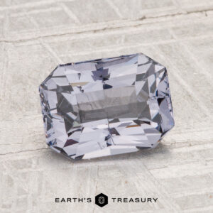 A rectangular, faceted light purple 2.07-carat Spinel gemstone is displayed on a textured gray surface with the "Earth's Treasury" logo at the bottom.