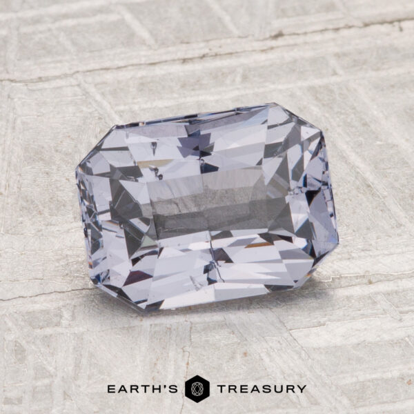 2.07-Carat Spinel A rectangular, faceted light purple 2.07-carat Spinel gemstone is displayed on a textured gray surface with the "Earth's Treasury" logo at the bottom.